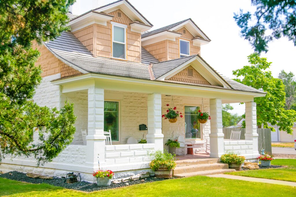 Cream And Tan Cottage With Painted Porch Cream and tan two-story cottage with white painted porch columns, cedar shake roof, and green shutters