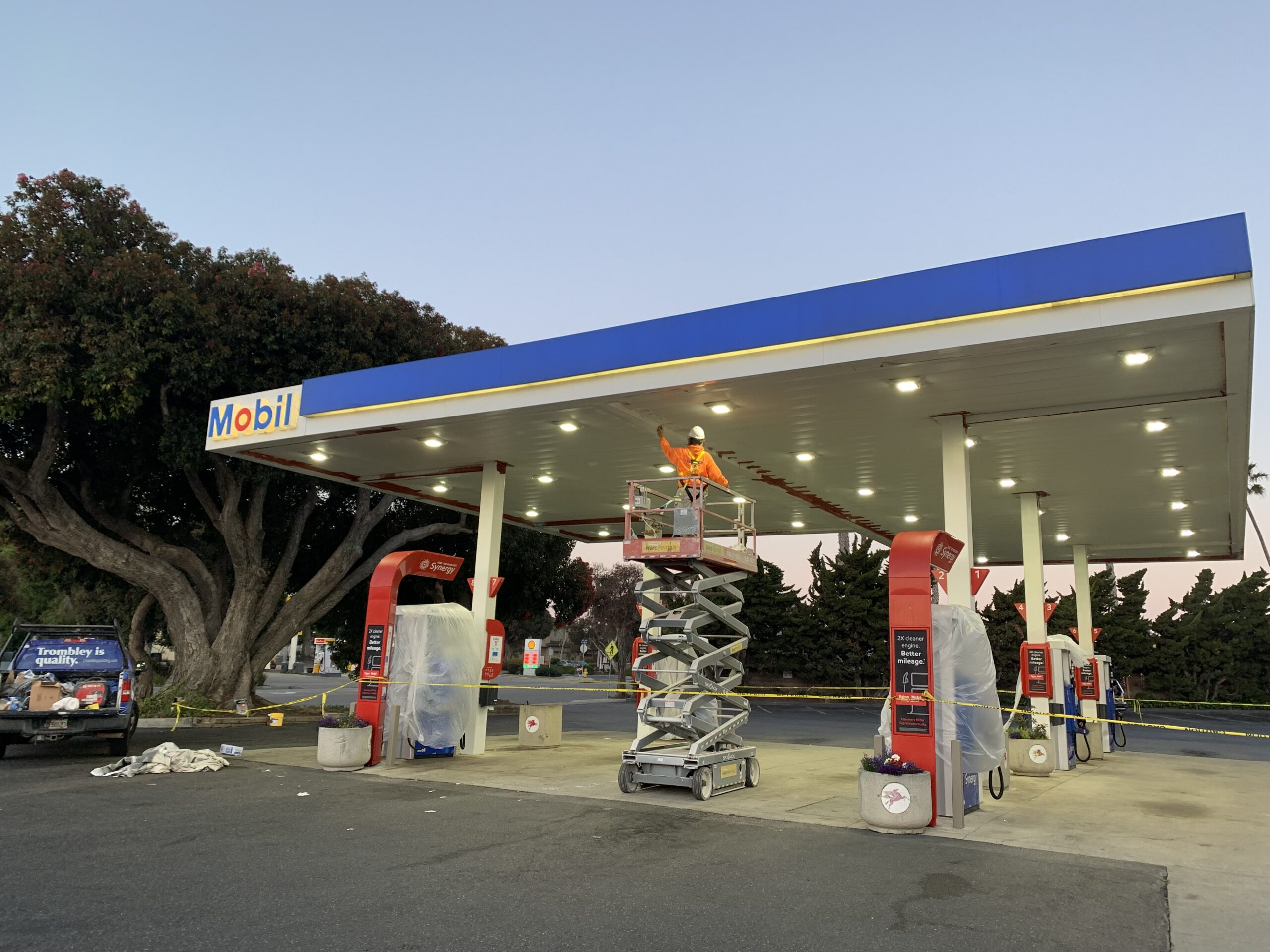 Commercial Gas Station Exterior Painting Services Painter on a scissor lift applying fresh paint to the canopy of a Mobil gas station.
