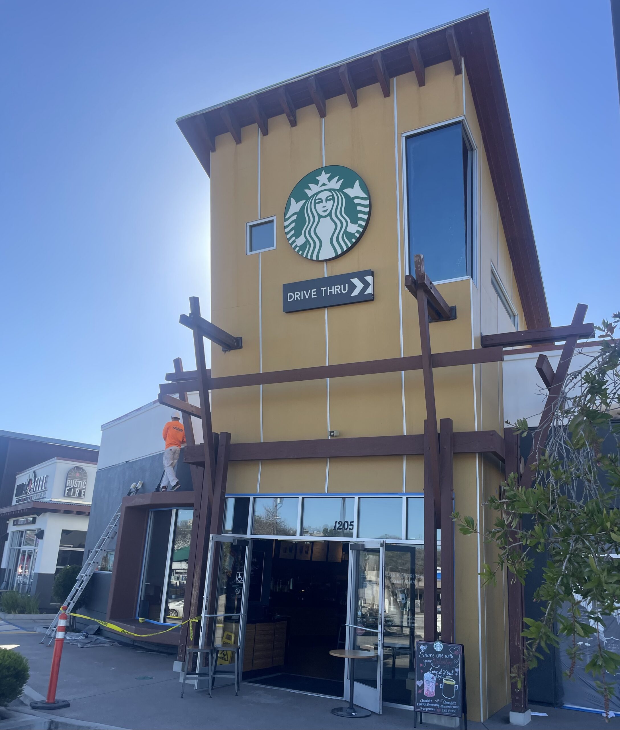 Commercial Exterior Painting for Retail Stores and Coffee Shops Painter on a ladder refreshing the exterior of a Starbucks coffee shop, highlighting commercial painting.