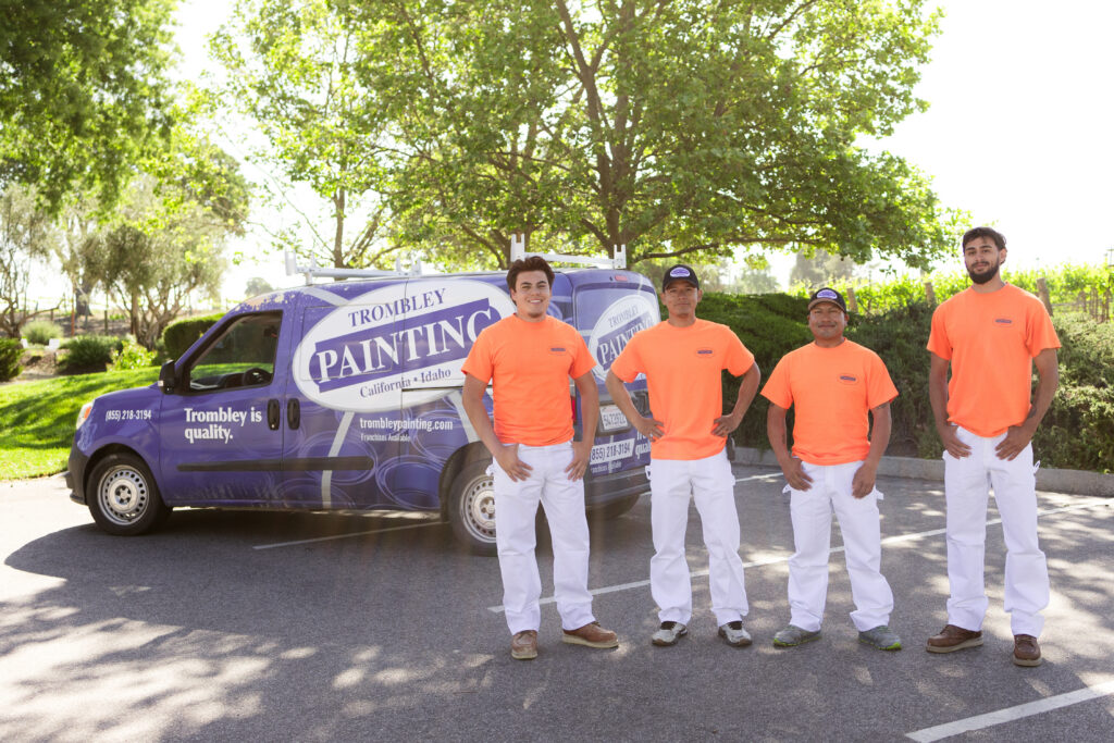 Professional Painting Crew for Residential and Commercial Projects Four professional painters from Trombley Painting stand proudly with their company van, ready for service.
